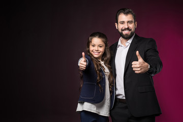 smiling father and daughter showing thumbs up on burgundy
