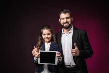 daughter holding tablet and father showing thumb up on burgundy