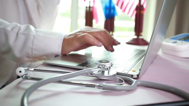 Doctor's writing and working on laptop computer, writing prescription clipboard with record information paper folders on desk in hospital or clinic, Healthcare and medical concept. Focus stethoscope