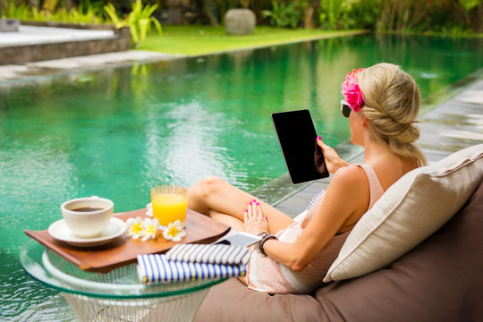 Woman using tablet while relaxing by exotic tropical pool