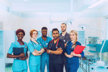 group of mixed-race medical students posing in the operating room. a multiracial team of doctors surgeons in suits with folders in hands smiling after the exam. office of the hospital background