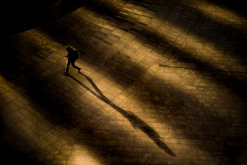 Ragazzo con zaino che cammina all’alba proiettando la sua ombra sul selciato deserto