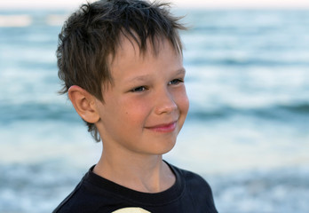 Portrait of a handsome boy with an Eupropean appearance. A sweet sunbathing baby boy smiles tenderly against the backdrop of the sea at sunset.