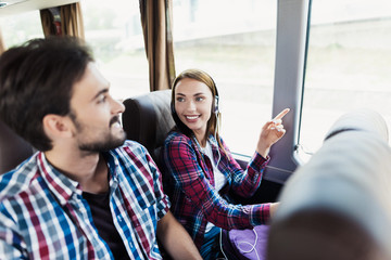 The guy and the girl are on the bus. The girl has headphones. He and the guy are discussing something and smiling.