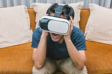 The man wearing virtual reality glasses sitting and scream on brown sofa, smartphone using with VR headset.