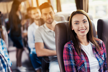 Woman posing on bus. She sits and smiles. Around her sit the other passengers.