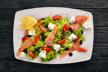 Salmon salad, feta cheese, salad leaves and fresh vegetables on the plate. On a wooden background. Top view. Free space for text.