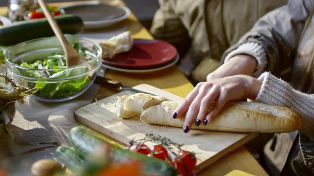 Closeup of female hands slicing bread on wooden cutting board at dinner table