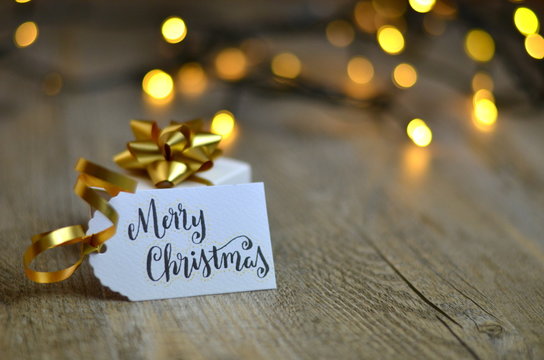 MERRY CHRISTMAS gift tag on wooden background with gift and bokeh lights