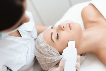 The doctor cleanses the woman's skin with a special medical device. The woman came to procedure of laser hair removal.