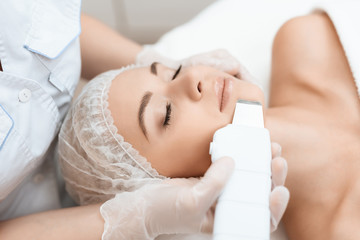 The doctor cleanses the woman's skin with a special medical device. The woman came to procedure of laser hair removal.