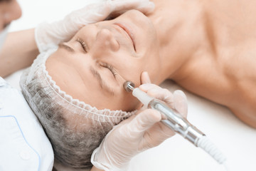 A man came to laser hair removal facial. Doctor leads him in the face with a modern laser epilator.