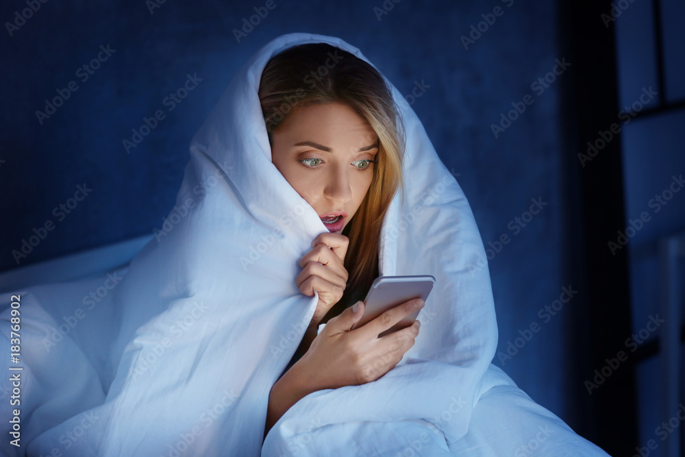 Wall mural emotional young woman with mobile phone in bed at night