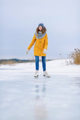 Young beautiful girl in yellow jacket is skating at winter on a frozen lake.