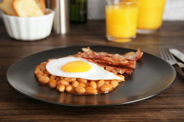 Plate with fried egg, bacon and beans on wooden table