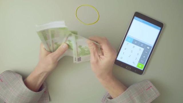 Top view. Male hands counts money and summarize the result on the calculator