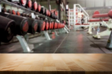 Obraz premium Wooden table on blurred background of fitness gym interior of modern club with equipment for your photomontage or product display.