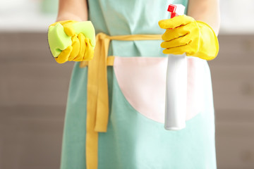 Woman holding bottle of detergent and sponge indoors