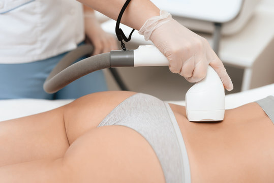 The woman came to the procedure of laser hair removal. The doctor treats her lower back with a device.