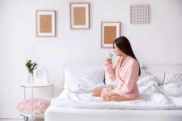 Obraz na płótnie Canvas Young woman drinking coffee while sitting on bed at home