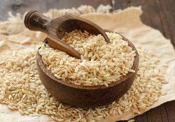 Pile of Brown rice in a bowl with a wooden spoon