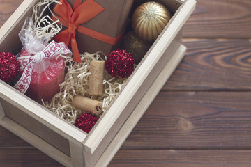 New year surprise in a wooden box with a yellow filler. A handcrafted brown gift box with an orange ribbon. a red wax candle in a plastic bag with ribbon, red and golden balls and cookies. Rustic
