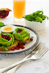 Toast with avocado rose, boiled egg and fresh salad on white table cloth