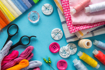 Multicolored threads, scissors, buttons, fabric and various sewing accessories on a blue background...