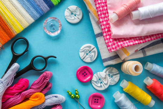 Multicolored threads, scissors, buttons, fabric and various sewing accessories on a blue background with copy space flat lay