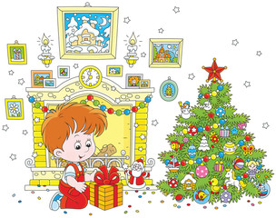 Little boy with his holiday gift near a fireplace and a colorfully decorated Christmas tree