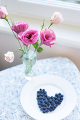 ripe blueberries in a heart shape on a table with flowers.