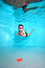Child underwater dives to the bottom of the pool after a toy on a blue background. Portrait. Shooting under water. Vertical orientation
