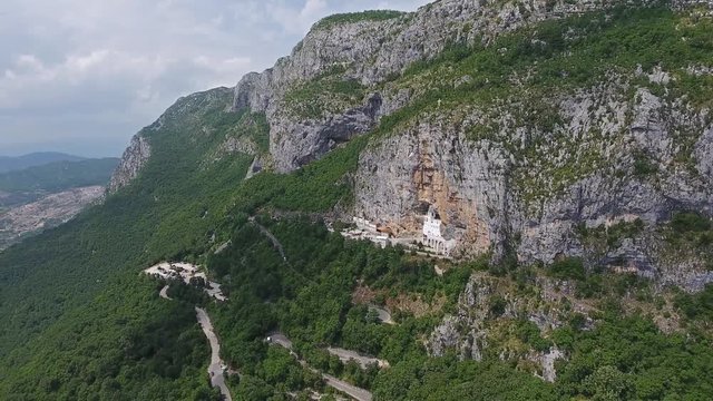Aerial panorama with Ostrog Monastery church under tall mountain walls, Montenegro, 4k
