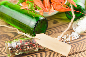 Lot of boiled red crayfishes and green fresh dill in white ceramic bowl beside two full bottles of beer and scattered salt and pepper and blank paper with rope on old rustic brown wooden planks