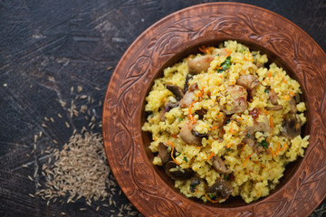 Clay plate with pilaf on a dark brown stone background, horizontal shot with space, view from above