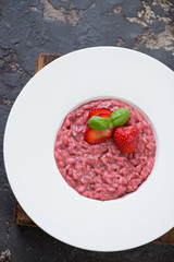 White plate with strawberry risotto over brown stone background, vertical shot, above view