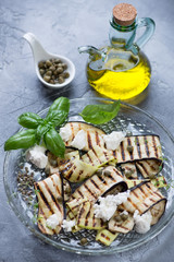 Grilled eggplants and zucchini with olive oil, capers and cheese on a grey stone background, vertical shot