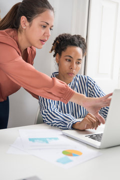 Two businesswomen meeting at office desk looking at laptop