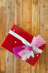 Red gift box and red ribbon and mini heart inside on wood background with space..