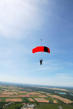 Skydiver is flying under parachute against sky over rural fields