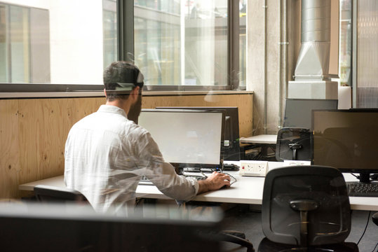 Rear view of man in office using desktop computer
