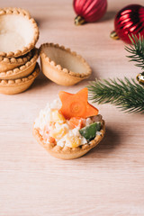 Crab salad tarts on wooden background. Christmas holiday buffet table served by snacks. Red baubles, fir-tree branches. 