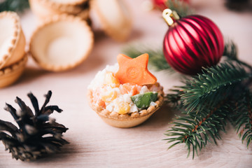 Fototapeta na wymiar Crab salad tarts on wooden background. Christmas holiday buffet table served by snacks. Red baubles, fir-tree branches. 