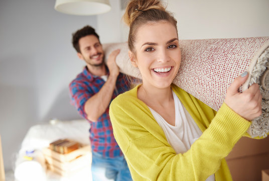 Young couple moving home, carrying rolled tug on shoulders, smiling