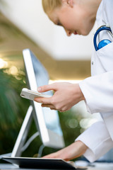 Female doctor holding smartphone, looking in diary, mid section