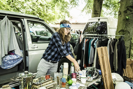 Female stall holder unpacking second hand cups on stall at forest flea market