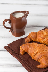Freshly baked croissants on brown napkin, cream in ceramic milk jug on white old wooden background. Fresh pastries for breakfast. Delicious dessert. Closeup photography. Vertical banner