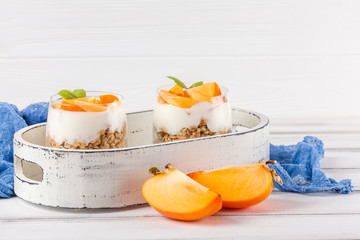 Persimmon creamy trifle in beautiful glasses, fresh ripe fruit slices on white wooden background. Healthy vegetarian food. Delicious dessert. Close up photography. Selective focus.