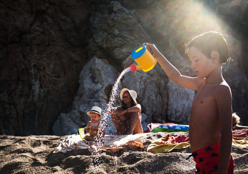 Boy on beach sprinkling toy watering can, Begur, Catalonia, Spain