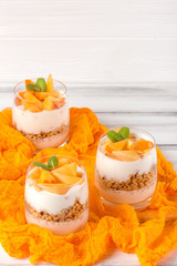 Persimmon creamy trifle in beautiful glasses, fresh ripe fruit slices on white wooden background. Healthy vegetarian food. Delicious dessert. Close up photography. Selective focus.